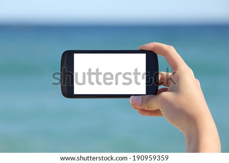 Woman hand showing a blank smart phone horizontal screen display on the beach with the sea in the background