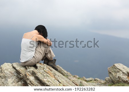 Depressed and sad woman alone in the mountain with a gray cloudy background