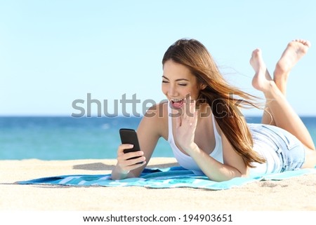 Teenager girl waving to the camera during a smart phone video call in vacations with the sea in the background