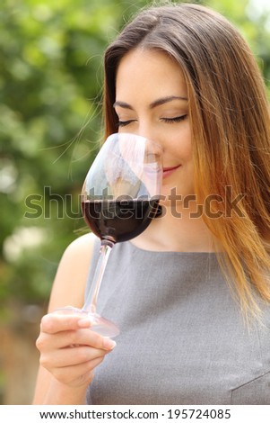 Somelier woman smelling and tasting red wine with a green background