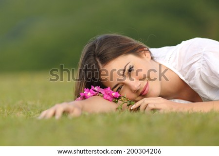 Relaxed woman resting on the green grass with flowers in a park with a green background