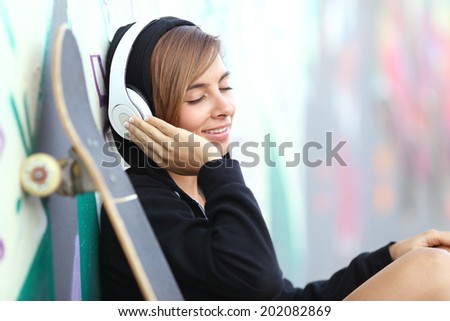 Skater teen girl listening to the music with headphones with blurred graffiti wall in the background