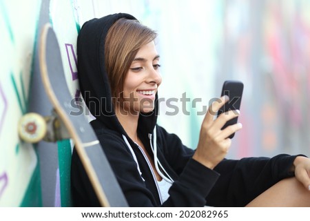 Young skater happy teen girl using a smart phone with a blurred graffiti wall in the background