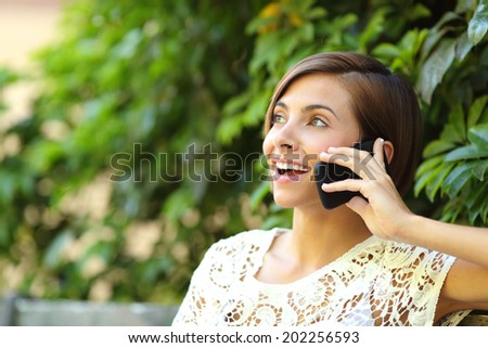 Casual happy woman on the phone in a park sitting on a bench with a green blurred background