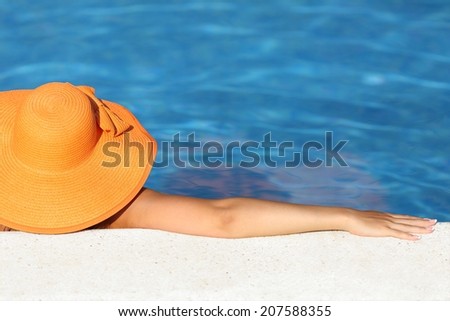 Woman with an orange picture hat bathing relaxed in a pool water enjoying vacations with blue background