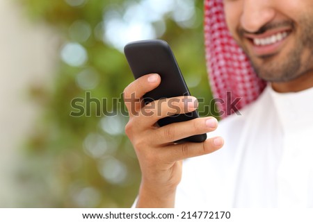 Smiling arab saudi man hand using a smart phone outdoor in a park with a green background