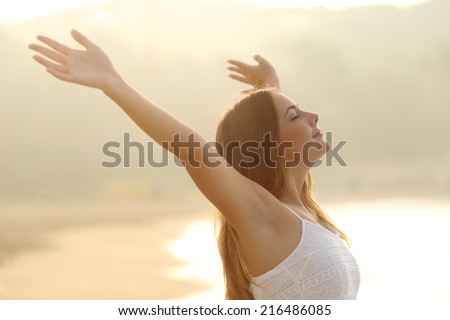 Relaxed woman breathing fresh air raising arms at sunrise with a warmth golden background