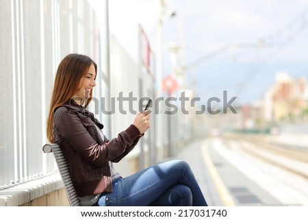 Happy woman texting on a smart phone in the train station with the railway in the background