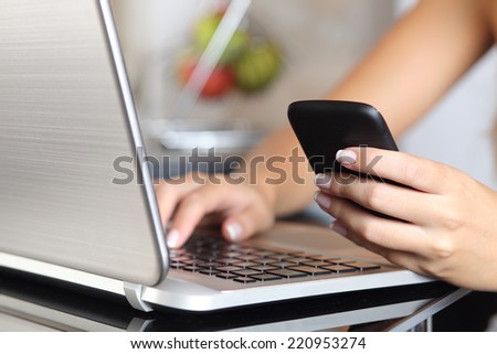 Close up of a woman hand using a smart phone and typing a laptop in the kitchen at home