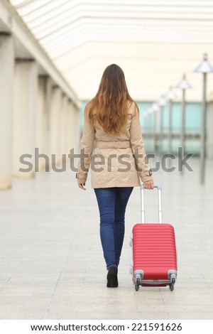 Back view of a tourist woman walking and carrying a suit case in an airport or station