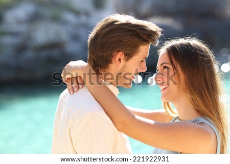 Couple in vacations looking each other ready to kiss with a turquoise water in the background