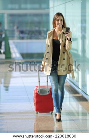 Front view of a traveler woman walking and using a smart phone in an airport corridor
