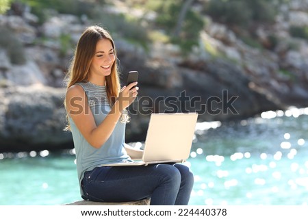 Entrepreneur woman working with a phone and a laptop on holidays in a tropical beach
