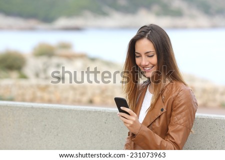 Happy woman using a smart phone on the beach with copy space and the sea in the background
