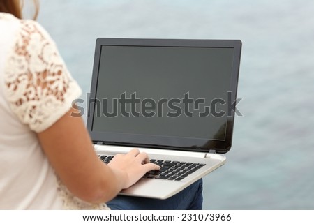 Woman working with a laptop and showing the display with the sea in the background