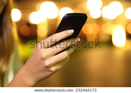 Close up of a woman hand using a smart phone in the night with lights in the background