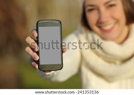 Happy woman showing a blank smart phone screen outdoors in winter