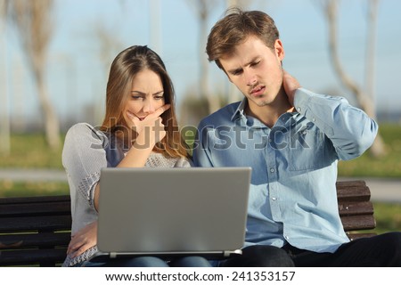 Worried students or entrepreneurs watching a laptop sitting on a bench in a park