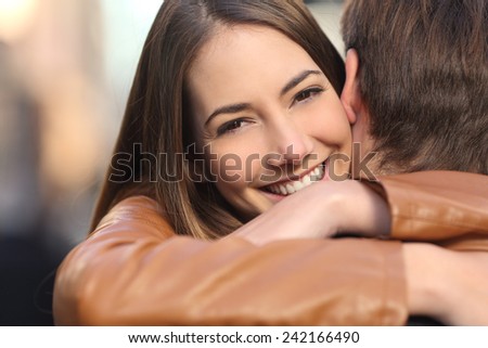Portrait of a happy girlfriend hugging her boyfriend and looking at camera
