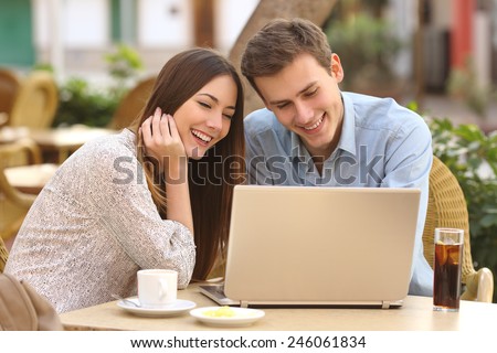 Happy couple watching social media in a laptop in a restaurant terrace
