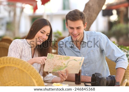Happy couple tourists consulting a guide in a restaurant terrace