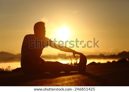 Silhouette of a fitness runner man stretching at sunset with the sun in the background