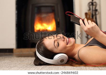 Woman listening to the music from a smartphone lying on the floor at home with a fireplace in the background