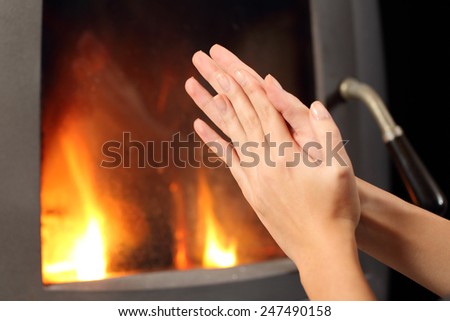 Woman rubbing hands and heating in front a fire place at home in winter