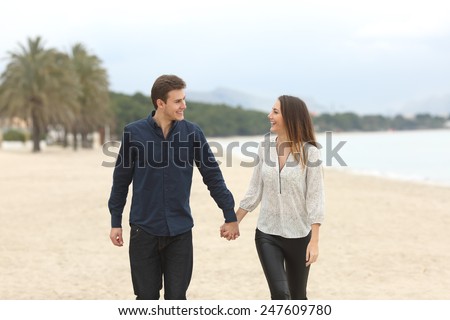Front view of a couple in love taking a walk and looking each other on the beach in winter