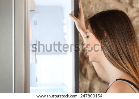 Woman opening the door of her empty fridge and looking inside