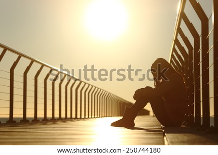 Sad teenager girl depressed sitting in the floor of a bridge on the beach at sunset