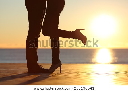 Couple legs silhouette hugging in love on the beach with the sun in the background at sunset