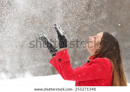 Woman wearing a red jacket throwing snow in the air in winter holidays