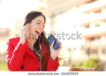 Funny girl listening to the music with earphones from a smart phone with an urban unfocused background