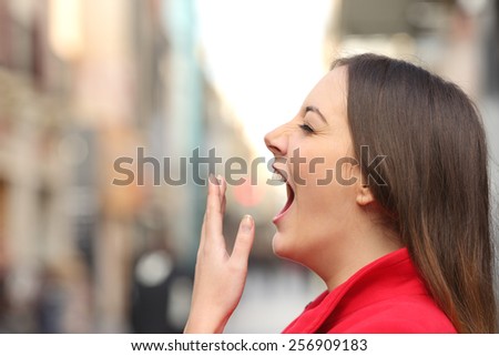 Tired woman yawning in the street in the morning with an unfocused urban background