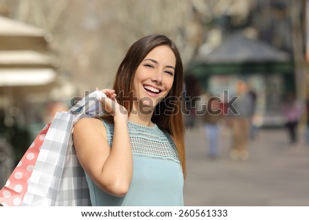 Happy consumer woman buying and holding shopping bags in the street of a city