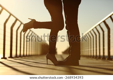 Back light of a couple legs silhouette hugging with love in a bridge at sunset