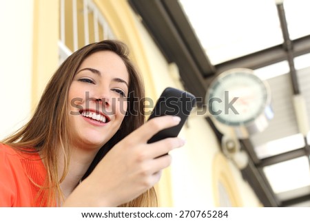 Woman using a mobile phone in a train station with a clock in the background