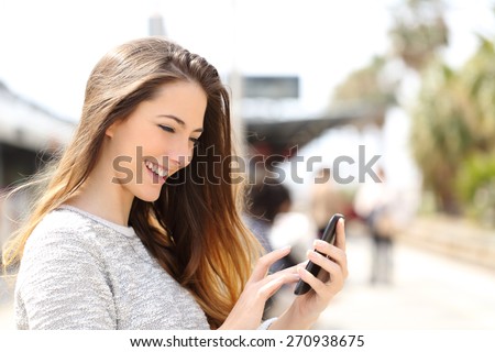 Happy girl texting on a smart phone in a train station while is waiting