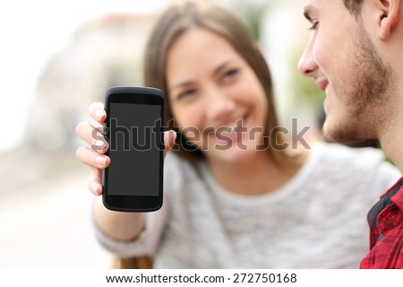 Happy couple showing apps in a blank smart phone screen outdoors