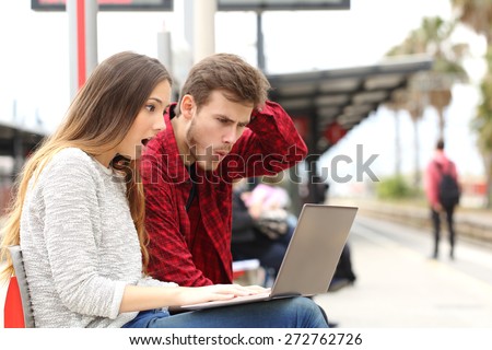 Couple worried and surprised watching a laptop in a train station while they are waiting