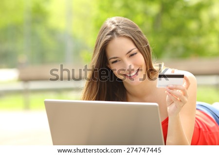 Shopper girl buying online with a laptop and credit card lying in a park in summer