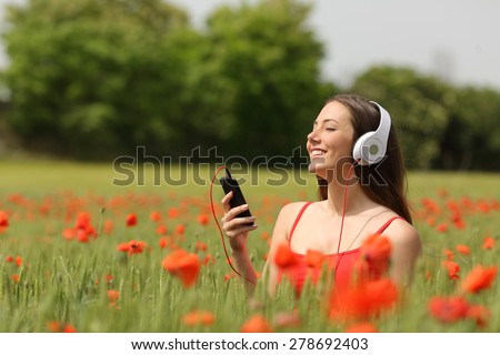 Relaxed woman breathing and listening music from a smart phone in a green field with red flowers in summertime