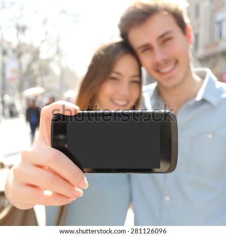 Happy couple or friends making a selfie photo with a smart phone and showing a blank screen to the camera