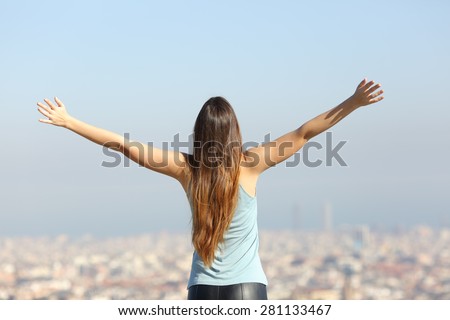 Back view of a happy tourist woman raising arms looking at the city landscape