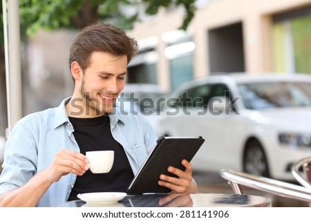 Happy man reading an ebook or tablet in a coffee shop terrace holding a cup of tea