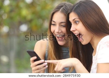 Euphoric friends watching videos on a smartphone and pointing at screen surprised