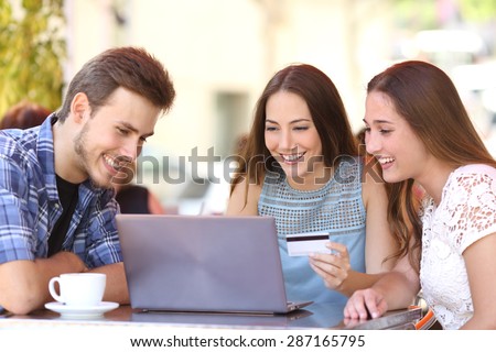Three happy friends shopping online with a credit card and a laptop in a coffee shop