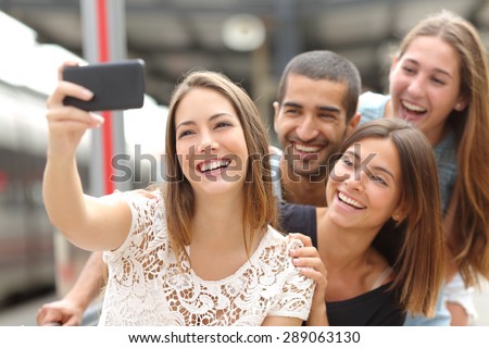Group of four funny friends taking selfie with a smart phone in a train station in summer