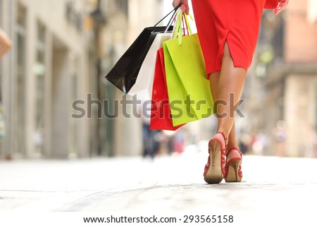 Back view of a fashion shopper woman legs walking with colorful shopping bags in the street